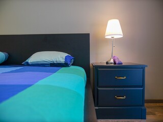 Sticker - Large bed with a blue green cover near a bedside cabinet with an illuminated lamp