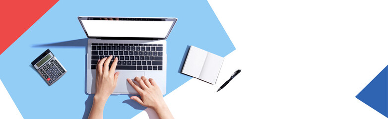 Person using a laptop computer with a notebook and a calculator