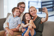 © Alex S/peopleimages.com - Family, happy and phone selfie on the sofa and smile for a social media post. Mother, father and kids together, bonding and carefree weekend in the living room and taking a picture with smartphone
