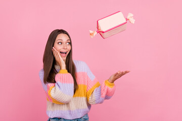 Poster - Photo of impressed positive lady arm catch throw candy giftbox touch cheek isolated on pink color background