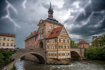 Das Bamberger Rathaus in der historischen Altstadt von Bamberg auf einer Insel im Fluß Regnitz bei Gewitterhimmel und zuckenden Blitzen