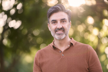 Close-up view of a relaxed middle-aged man looking at camera while standing outdoors in a park.