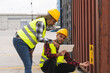 © Marc - Female worker in safety clothes pointing at her coworker's tablet screen in the vicinity of a port