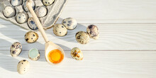 Broken Quail Egg With Bright Orange Yolk In Wooden Spoon Among Whole Quail Eggs. Space For Text