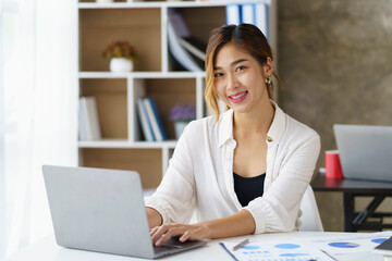 Wall Mural - Portrait of smiling Asian businesswoman enjoying work diligently using her laptop computer at the office.