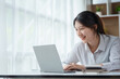 © amnaj - Portrait of smiling Asian businesswoman enjoying work diligently using her laptop computer at the office.