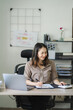 © Kritdanai - Portrait of a beautiful Asian woman looking at laptop screen while sitting at working desk in the office