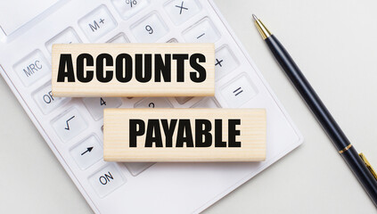 Wooden blocks with the ACCOUNTS PAYABLE Iie on a light background on a white calculator. Nearby is a black handle. Business concept