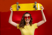 Happy Woman Holding Skateboard Overhead In Front Of Red Wall