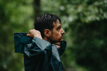 Man Wearing A Raincoat Putting On His Hood In The Middle Of A Forest