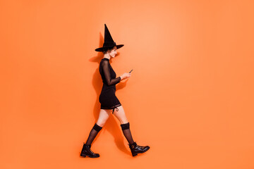 Wall Mural - Full length profile photo of magician person walking hold use telephone isolated on orange color background