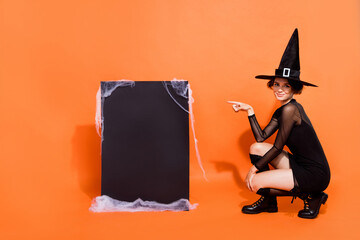 Wall Mural - Full body photo of charming witch lady indicate finger empty space placard isolated on orange color background
