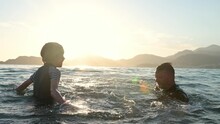 Happy Child And His Mature Father Having Fun Together During Swim In The Sea At Sunset. Joyful Boy And His Dad Splashes With Water While Swimming In The Lake.Active Leisure For Family During Holidays