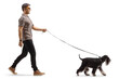 Full length profile shot of a cool young man walking a schnauzer dog on a lead