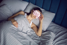 Woman In A Pink Eye Mask Lies Under A Blanket In A Bed And Suffers From Insomnia.