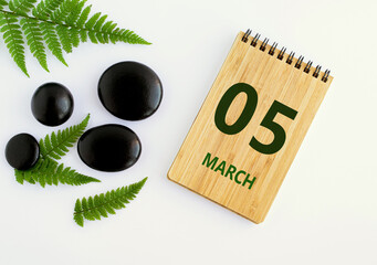 Wall Mural - March 05. 05th day of the month, calendar date. Notepad, black stones, green leaves. Spring month, the concept of the day of year