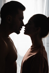 dark silhouettes of woman in t-shirt and shirtless man standing face to face and looking at each other.