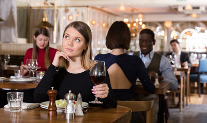 Wall Mural - Portrait of thoughtful attractive girl with wine glass dining all alone in cozy restaurant .