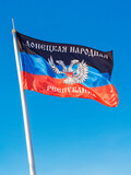 Fototapeta Miasto - Flag of Donetsk People's Republic (DPR or DNR) with coat of arms in the center. Vertical against blue sky background. War in eastern Ukraine (Donbas) concept.