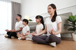 © tigercat_lpg - Happy Asian Thai family, parents, and children sit on living room floor, close their eyes together, tranquil meditate in lotus position, and practice healthy yoga, domestic home lifestyle weekend.