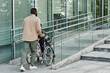 © Seventyfour - Back view of adult man assisting partner in wheelchair going up accessibility ramp in city, copy space