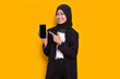 © dwi - young beautiful asian muslim business woman demonstrating mobile cell phone isolated on yellow background