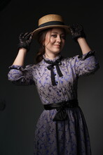 A Beautiful Woman In A Romantic Dress Of The 19th Century. Retro Style, With A Straw Hat And Lace Gloves. Historical Reconstruction. Romantic Lady Countess In A Dark Room. High Quality Photo