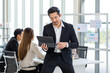 © Bangkok Click Studio - Millennial Asian professional successful bearded male businessman in formal suit sit on table browsing surfing internet via tablet computer in company office meeting room while colleagues discussing