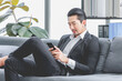 © Bangkok Click Studio - Millennial Asian professional successful bearded male businessman ceo director entrepreneur in formal suit relaxing take coffee break sitting crossed legs surfing browsing internet via smartphone