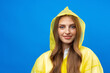 Young blonde woman wearing yellow raincoat smiling at camera over blue background in studio