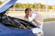 © Ivan Traimak - a woman driver in bewilderment, putting her hands to her head, looks at the engine of a broken car