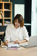 © Prathankarnpap - Focused asian woman employee working with laptop and checking financial reports on wooden office desk