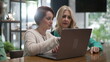 © Marco - Female executive woman explaining job to young female employee in front of laptop at cafe. Female entrepreneur in conversation with staff