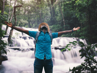 Wall Mural - Freedom african traveler man with backpack enjoying amazing tropical waterfall raising hands travel lifestyle and success vacation concept enter nature forest mountain background