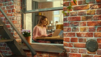 Poster - Portrait of a Young Woman Working on Laptop Computer while Sitting at Home in a Multi-Storey Brick House. Motivated Female Smiling and Feeling Happy while Working from Home. Zoom Out Shot.