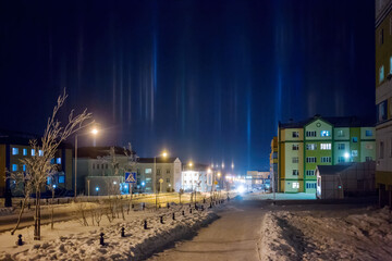 Wall Mural - Night cityscape. View of a snow-covered street in the northern city. Bright pillars of light in the frosty sky. Cold winter weather. City of Anadyr, Chukotka, Siberia, Far North of Russia. Arctic.