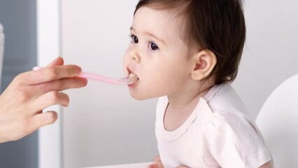 baby girl eating blend mashed food sitting, on high chair, mother feeding child, hand with spoon for