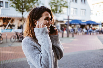 Wall Mural - Young happy woman talking on cell phone downtown