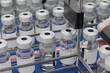 Rows of labelled glass vials on a conveyor with a generic Covid-19 vaccine. Factory setting. Blurred background.