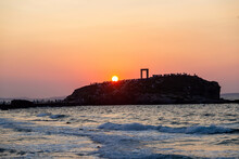 Naxos Island, Sunset Over Temple Of Apollo, Cyclades Greece. Visitors Admire The Sundown Background.