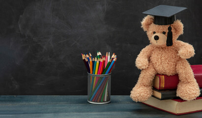 Wall Mural - Back to school. Teddy bear with graduation cap books and pencils on desk