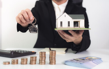 Fototapete - Home buying and Mortgage concept ; Financial man bank hold key and house model on front with coin money banknote and calculator
