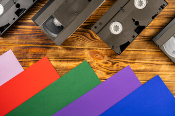 Wall Mural - Black vintage VHS videotapes on brown wooden background. Plastic retro video cassettes with analog magnetic tape from 90s on red, blue, green, purple and pink background. Nostalgia concept. Top view.