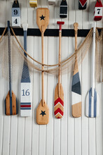 Several Colorful Wooden Paddles Hang On A White Wall Or Fence. Canoe Paddles For Active Water Sports Decorative.