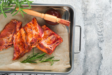 Pork ribs. Raw meat. Raw pork ribs in marinade with spices, rosemary, tomato sauce and garlic on old wooden stand on black stone table background. Barbecue concept. Top view. Mock up.