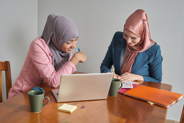 Two muslim business women wearing hijab working in a laptop. Businesswoman at work.