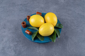 Wall Mural - Three organic lemons and leaves on blue plate