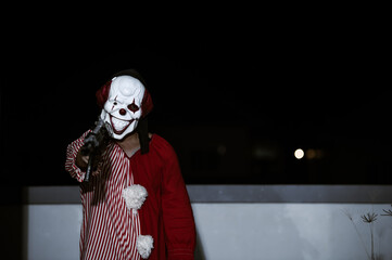 Asian handsome man wear clown mask with weapon at the night scene,Halloween festival concept,Horror scary photo of a killer in orange cloth,Evil clown charactor