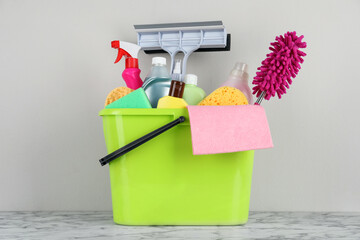 Light green bucket with cleaning products on marble table