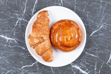 Wall Mural - Homemade sweet bun and croissant on the plate, on the marble background